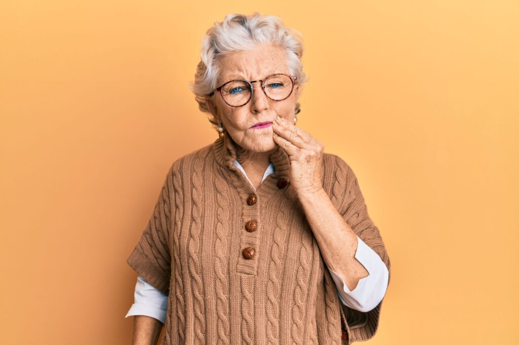 An older woman holding her face from tooth pain